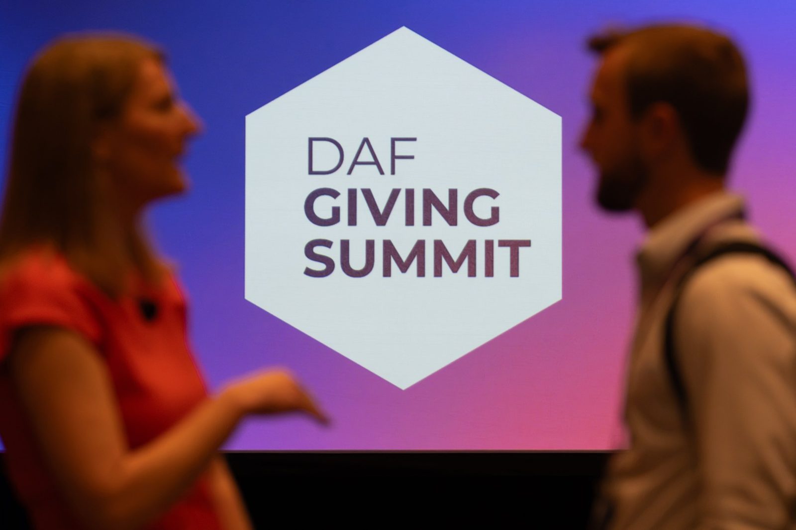Two attendees talking in silhouette in front of the DAF Giving Summit logo
