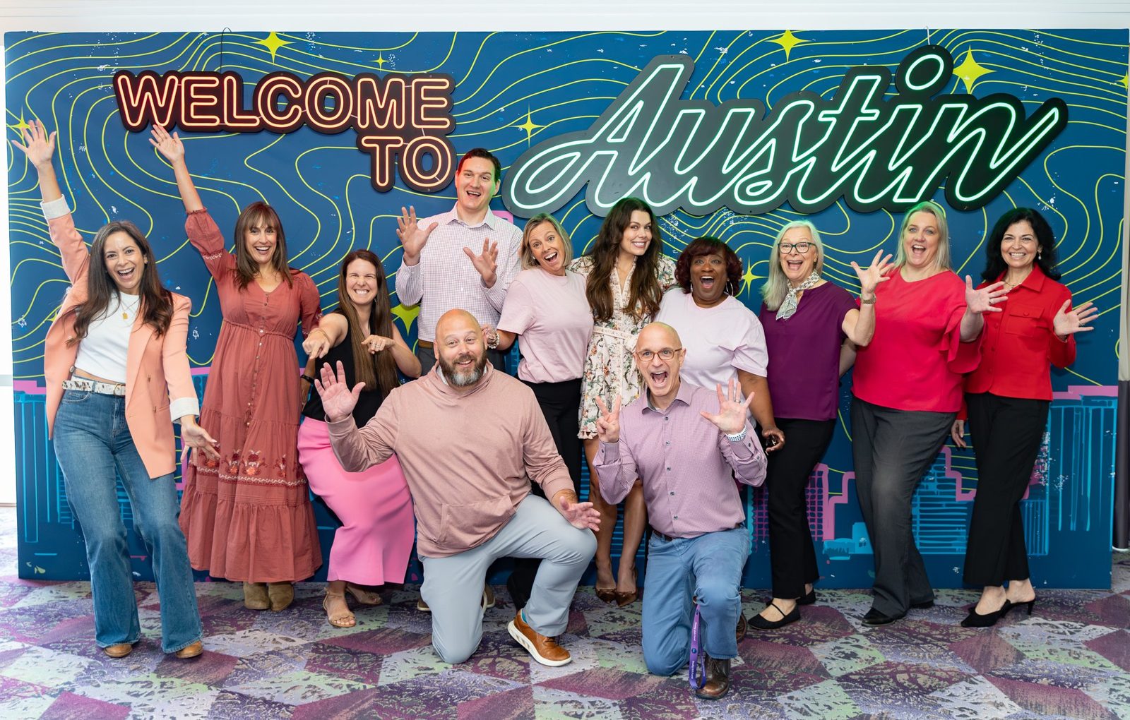 The event team cheering together in front of a Welcome to Austin neon backdrop